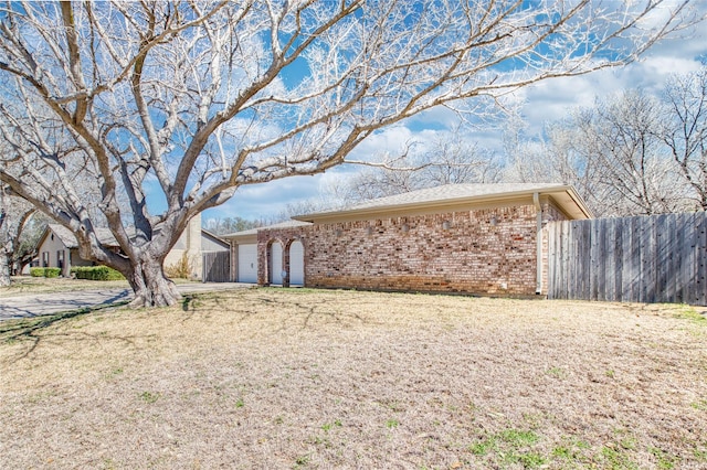 view of side of property with an attached garage, driveway, fence, and brick siding