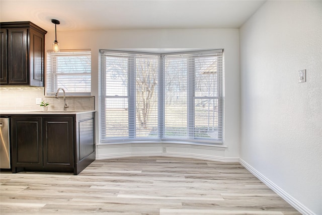 kitchen featuring dark brown cabinetry, light wood finished floors, a sink, light countertops, and backsplash