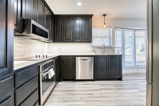 kitchen featuring appliances with stainless steel finishes, a sink, light wood-style flooring, and tasteful backsplash