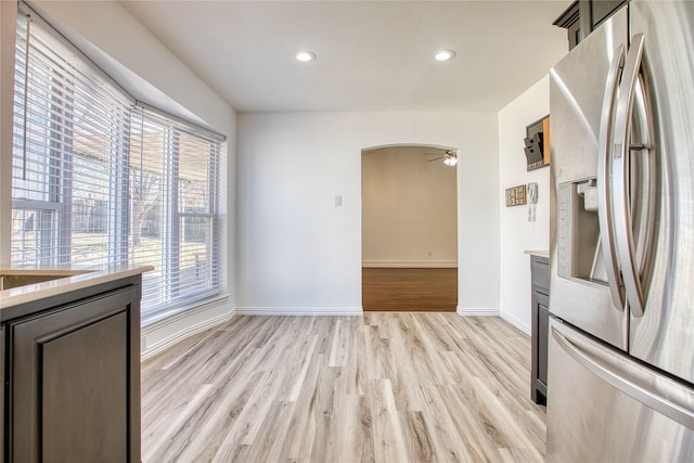 kitchen featuring arched walkways, light countertops, stainless steel refrigerator with ice dispenser, and light wood-style floors