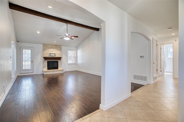 unfurnished living room with arched walkways, a fireplace, visible vents, lofted ceiling with beams, and wood finished floors