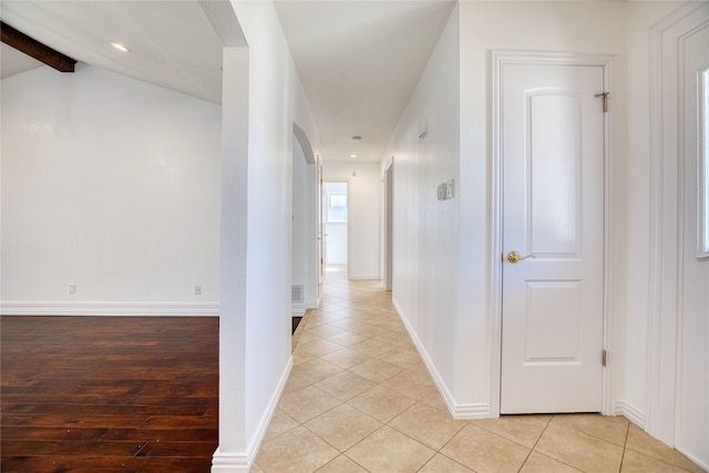 hallway with lofted ceiling with beams, light tile patterned floors, baseboards, and arched walkways