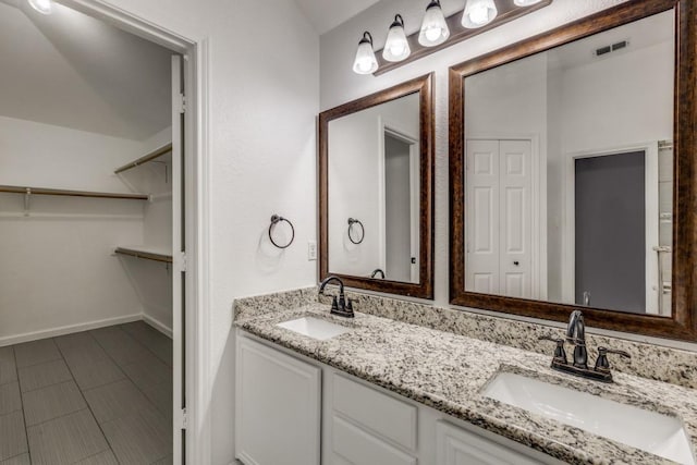 bathroom featuring visible vents, a sink, a spacious closet, and double vanity