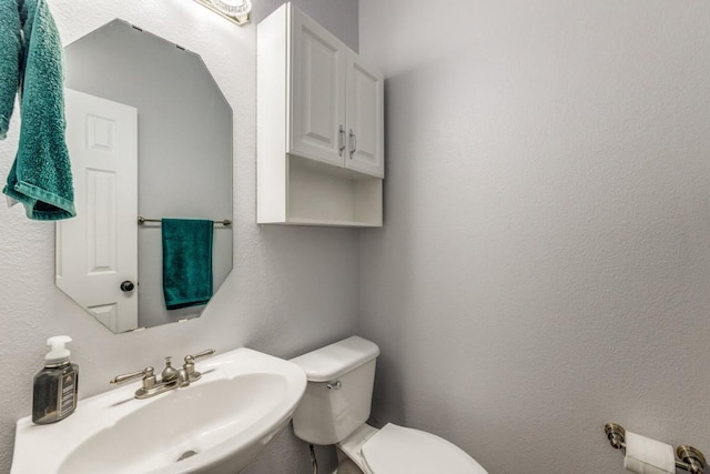 bathroom featuring toilet, a sink, and a textured wall