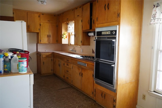 kitchen featuring dobule oven black, a sink, light countertops, freestanding refrigerator, and tasteful backsplash