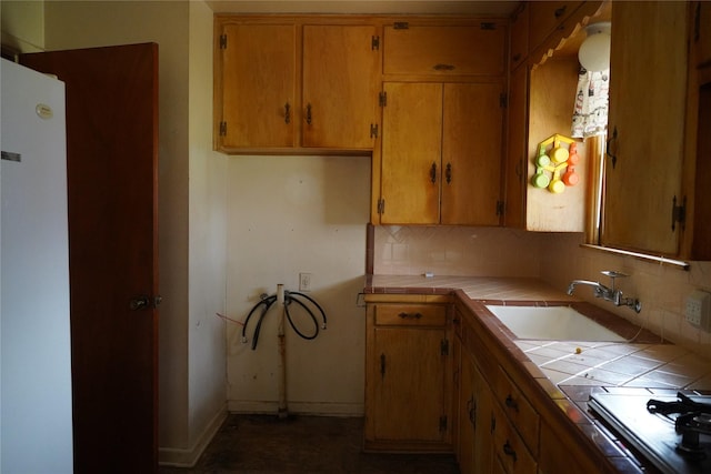 kitchen featuring tile countertops, decorative backsplash, brown cabinetry, a sink, and baseboards