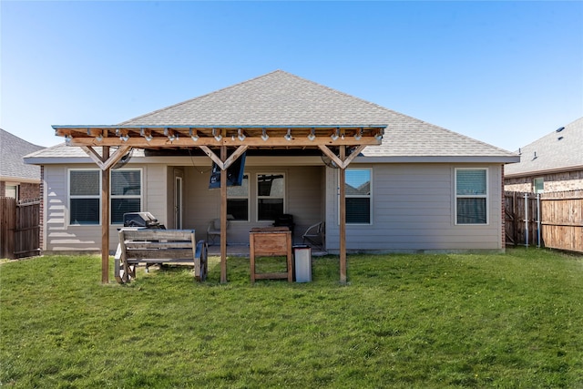 rear view of house with a yard, roof with shingles, and fence