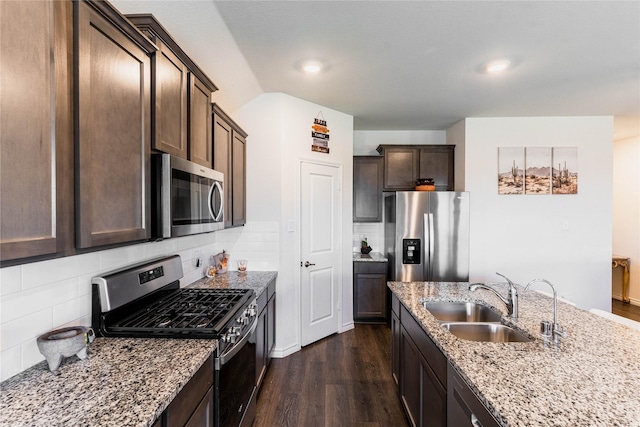 kitchen featuring light stone counters, stainless steel appliances, dark wood-type flooring, a sink, and dark brown cabinets