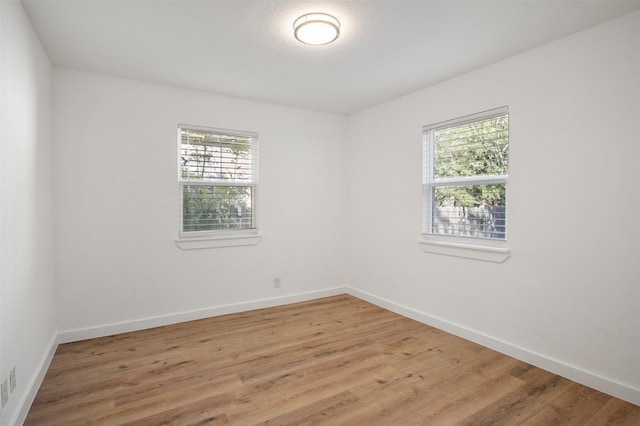 spare room with a healthy amount of sunlight, light wood-type flooring, visible vents, and baseboards