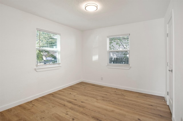 unfurnished room featuring a textured ceiling, light wood-type flooring, and baseboards