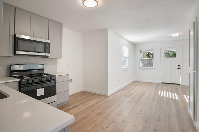 kitchen featuring black range with gas cooktop, stainless steel microwave, light countertops, and backsplash