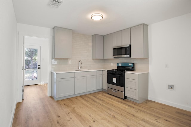 kitchen with light wood-style flooring, a sink, gray cabinets, stainless steel microwave, and gas range