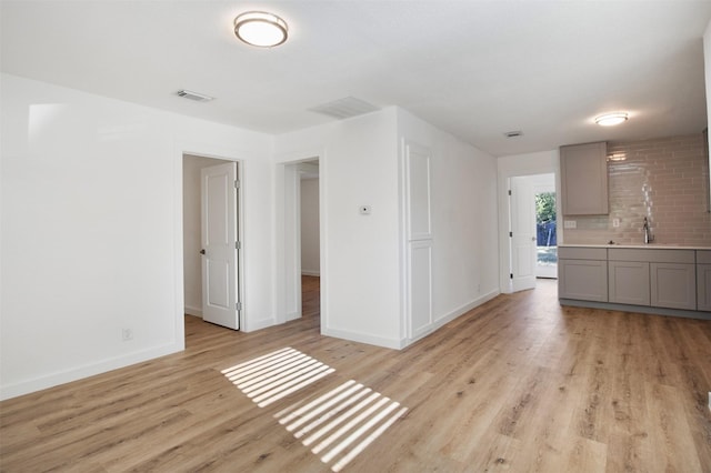 unfurnished room with light wood finished floors, a sink, visible vents, and baseboards