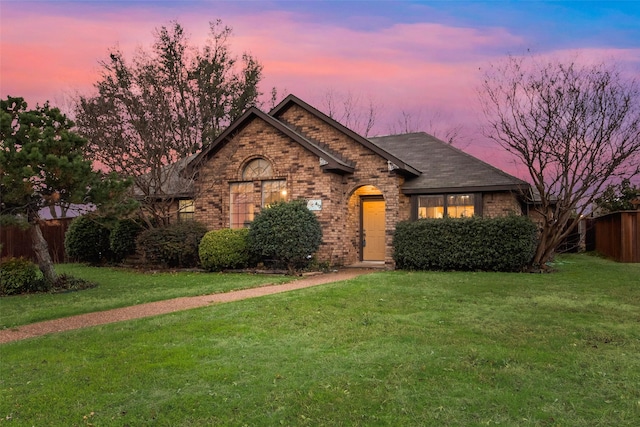 ranch-style house with roof with shingles, brick siding, a lawn, and fence