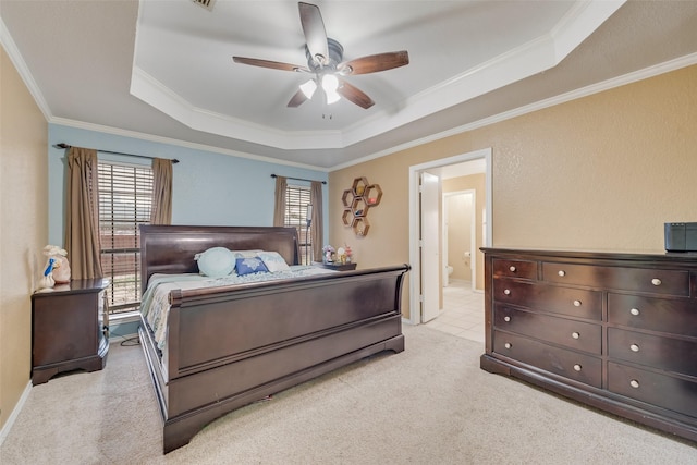 bedroom with connected bathroom, a tray ceiling, light colored carpet, and crown molding