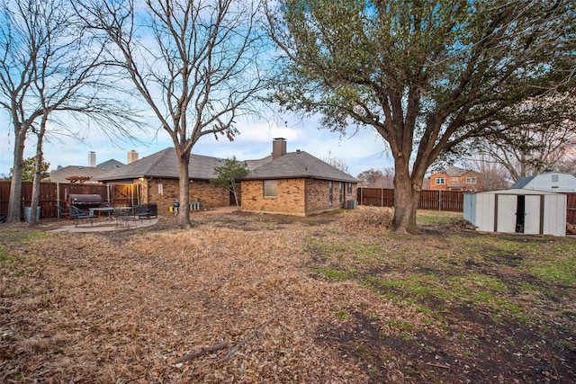 rear view of house with a patio, a fenced backyard, an outbuilding, a storage unit, and brick siding