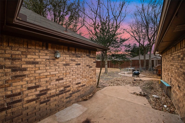 property exterior at dusk with fence, a patio, and brick siding