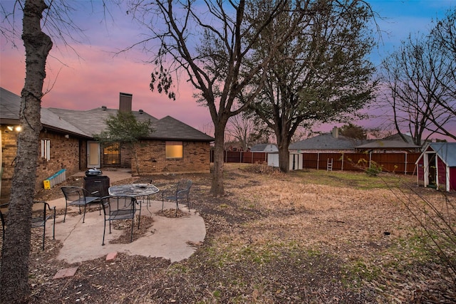 yard at dusk with a patio, a storage unit, an outdoor fire pit, fence, and an outdoor structure