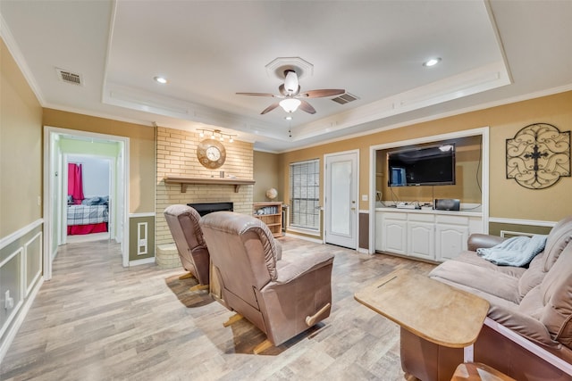 living room featuring a brick fireplace, a raised ceiling, visible vents, and crown molding