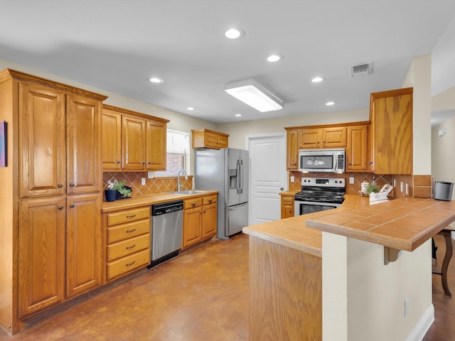 kitchen featuring visible vents, tile counters, a peninsula, stainless steel appliances, and a sink