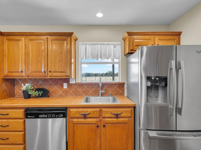 kitchen featuring tasteful backsplash, tile countertops, appliances with stainless steel finishes, brown cabinets, and a sink