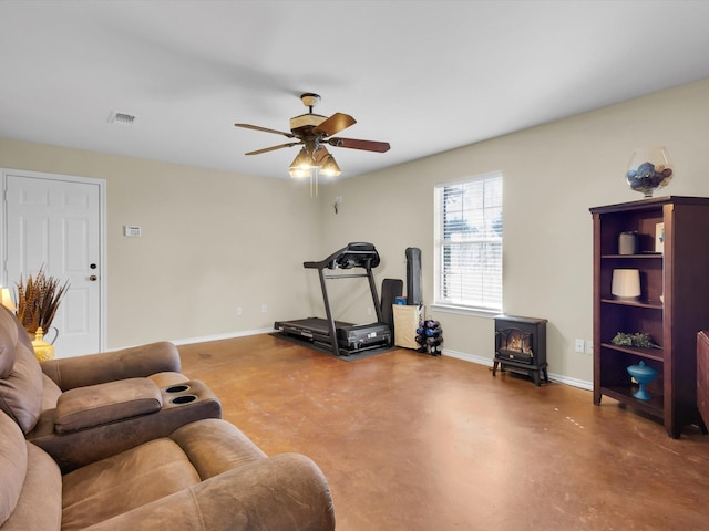 exercise area with a wood stove, baseboards, visible vents, and ceiling fan