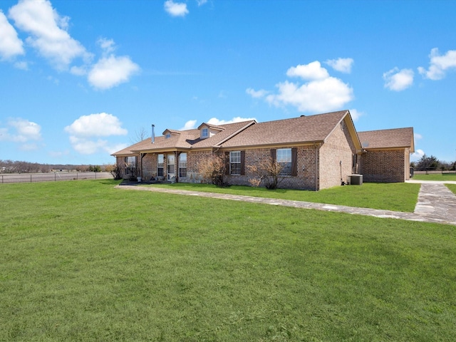 single story home with a shingled roof, a front lawn, central AC, and brick siding