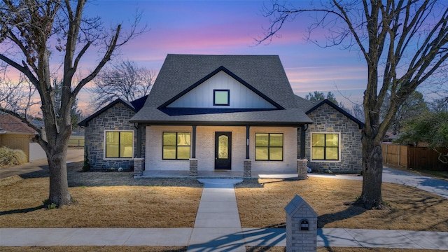 view of front of home featuring covered porch, brick siding, fence, roof with shingles, and board and batten siding