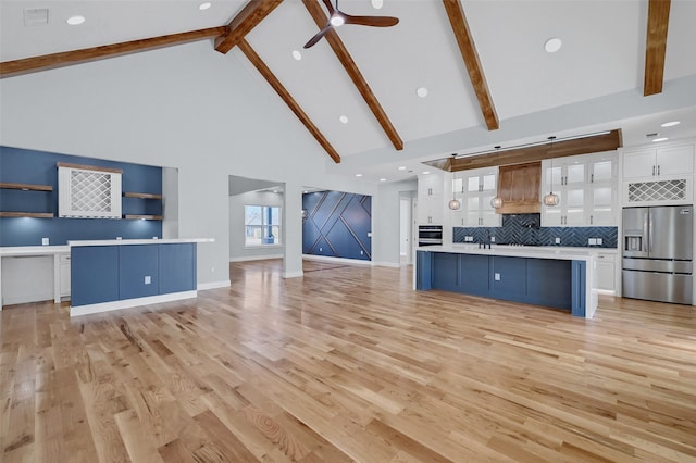 unfurnished living room featuring beam ceiling, light wood-style flooring, a ceiling fan, high vaulted ceiling, and baseboards