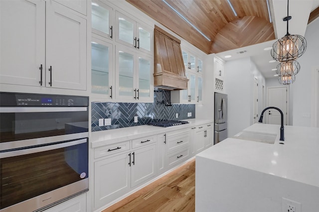 kitchen with tasteful backsplash, custom range hood, appliances with stainless steel finishes, hanging light fixtures, and a sink