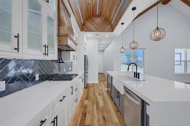 kitchen with custom exhaust hood, backsplash, appliances with stainless steel finishes, white cabinetry, and a sink