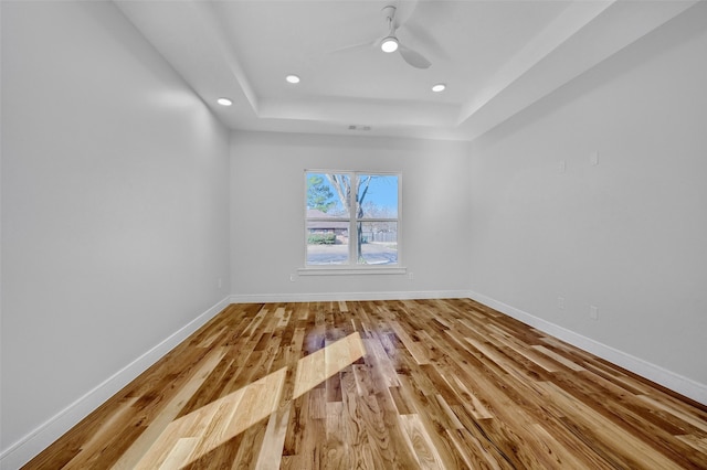 spare room featuring recessed lighting, a raised ceiling, baseboards, and wood finished floors