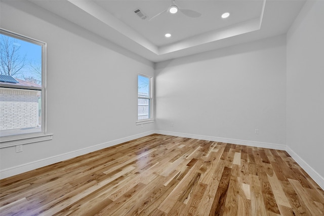 unfurnished room featuring light wood-style flooring, a raised ceiling, visible vents, and baseboards