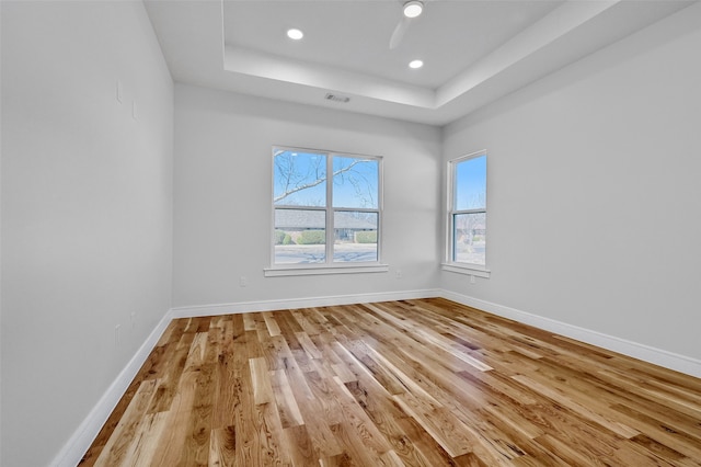 unfurnished room with recessed lighting, visible vents, baseboards, a tray ceiling, and light wood finished floors