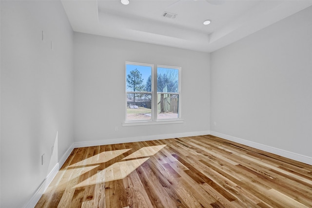 unfurnished room featuring baseboards, visible vents, a raised ceiling, and wood finished floors