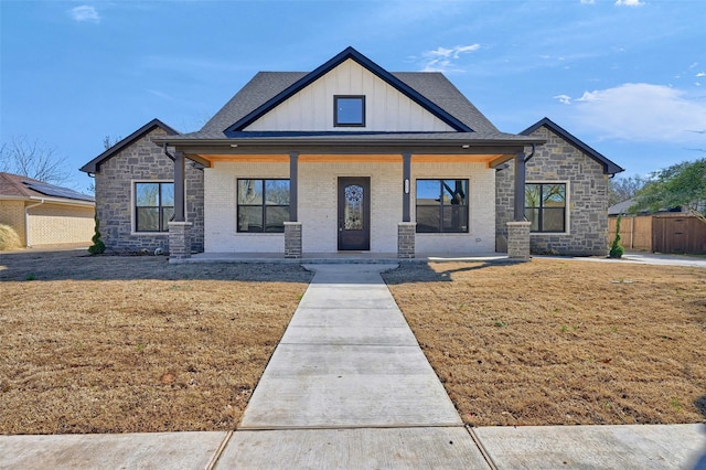 modern inspired farmhouse featuring brick siding, a shingled roof, a porch, board and batten siding, and a front yard