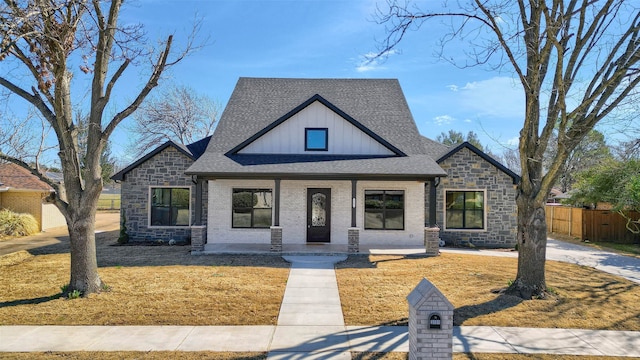 modern farmhouse featuring roof with shingles, covered porch, fence, board and batten siding, and brick siding