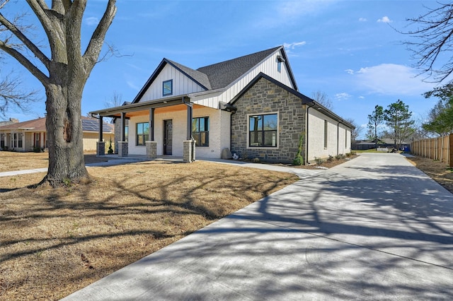 modern inspired farmhouse with a porch, central air condition unit, fence, stone siding, and board and batten siding