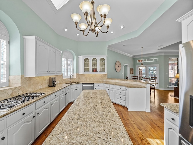 kitchen featuring a peninsula, wood finished floors, white cabinets, stainless steel appliances, and a sink