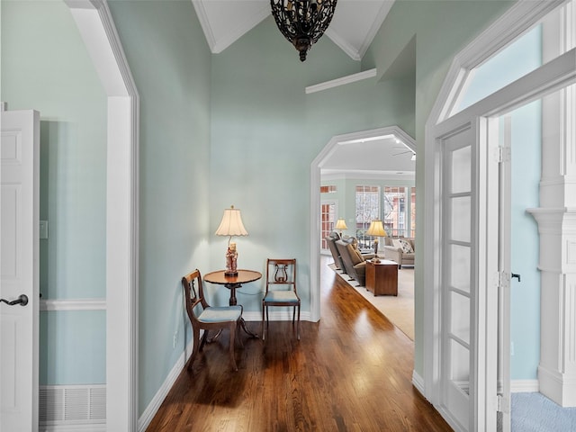 hall with wood finished floors, baseboards, lofted ceiling, arched walkways, and ornamental molding