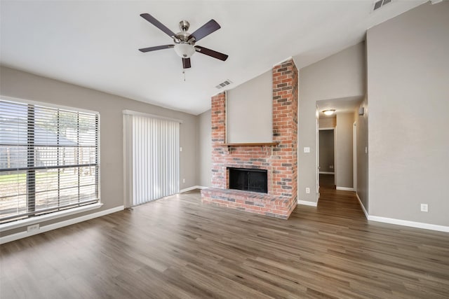 unfurnished living room featuring visible vents, a brick fireplace, vaulted ceiling, wood finished floors, and baseboards