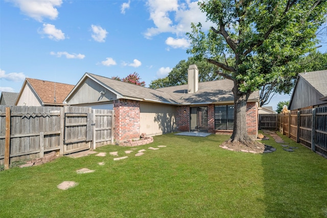 rear view of property with a lawn, a fenced backyard, a chimney, an attached garage, and brick siding