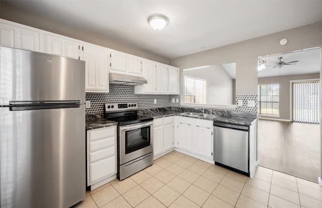 kitchen with light tile patterned floors, under cabinet range hood, stainless steel appliances, a sink, and white cabinetry