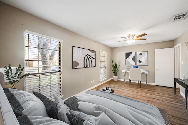 bedroom with multiple windows, wood finished floors, visible vents, and baseboards