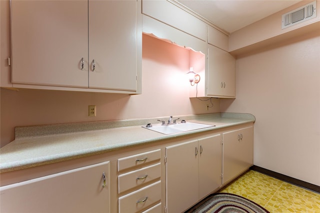 kitchen featuring light floors, light countertops, visible vents, white cabinetry, and a sink