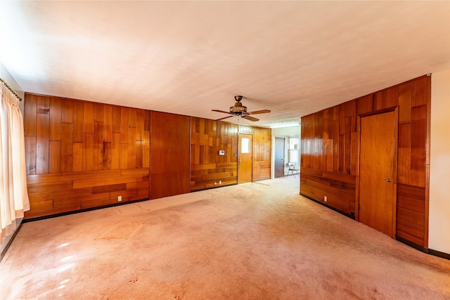 carpeted spare room featuring a ceiling fan and wooden walls