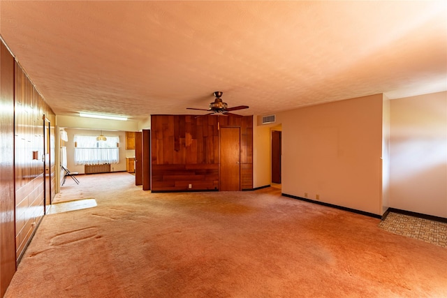 unfurnished living room with baseboards, visible vents, a ceiling fan, light colored carpet, and radiator