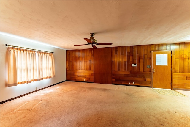 carpeted empty room with a textured ceiling, wood walls, a ceiling fan, and baseboards