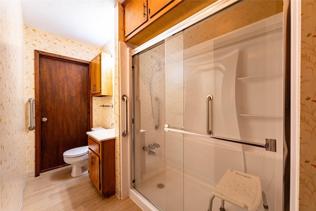 bathroom featuring toilet, vanity, a shower stall, wood finished floors, and wallpapered walls