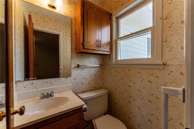 half bath featuring vanity, toilet, and wallpapered walls